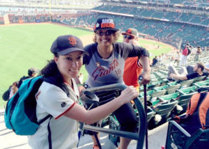 Two smiling women are in the stands at a baseball game.