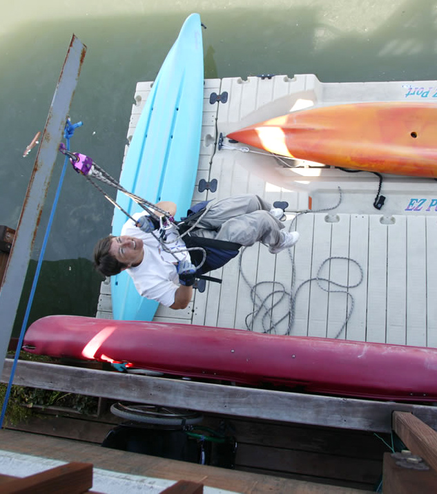 A female wheelchair user is being lowered from a crane into her kayak.